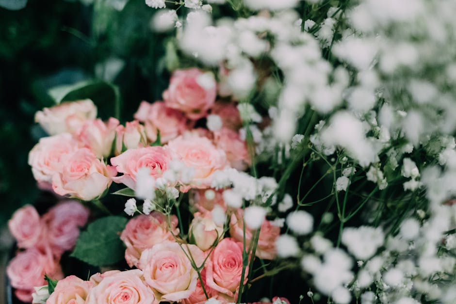 A close-up arrangement of fresh pink roses with tightly formed petals and green stems, complemented by delicate white baby's breath flowers scattered throughout. The roses are arranged in a lush bouqu